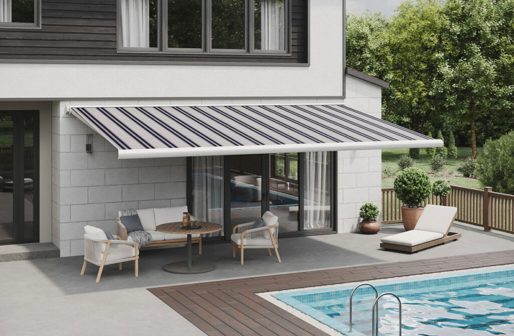 A modern patio with a round table and four chairs under a striped retractable awning, next to a pool. A lounge chair sits nearby, and trees and greenery surround the area.