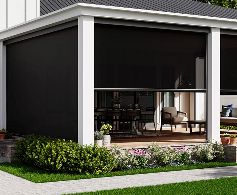 A modern house with a covered patio enclosed by dark retractable screens, outdoor seating and dining areas visible through the screens, surrounded by green lawn and shrubs.